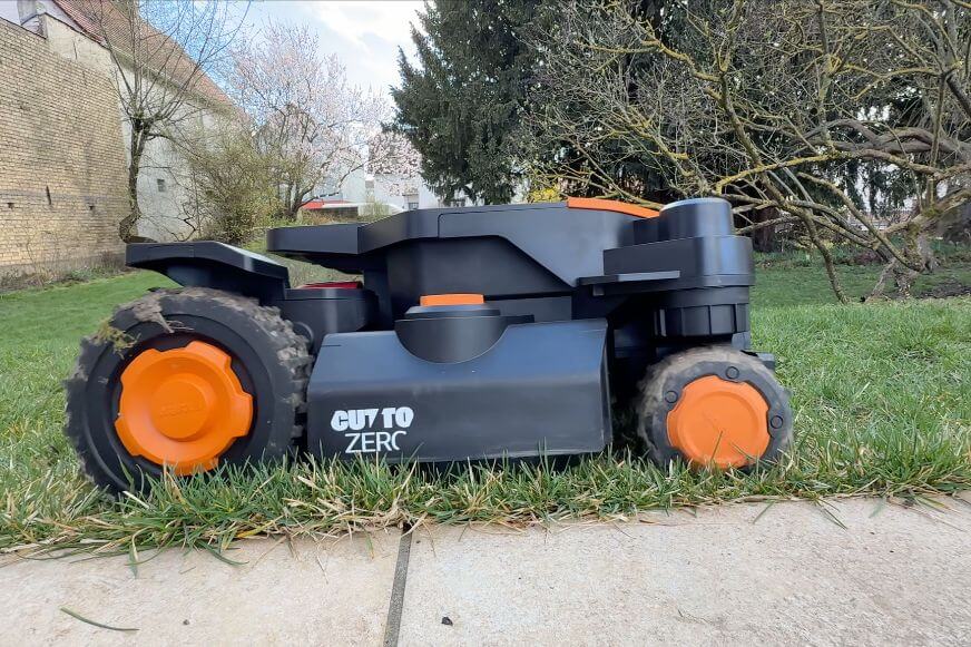 Sichtbarer Reststreifen aus ungemähtem Gras entlang einer Gartenmauer neben einem Mähroboter